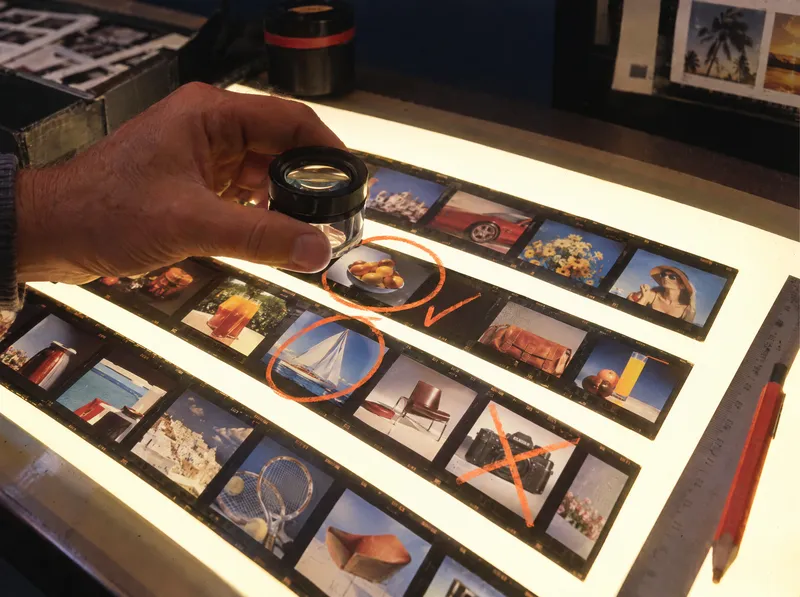 Photo années 80 : des visuels contrôlés à la loupe sur une table lumineuse.